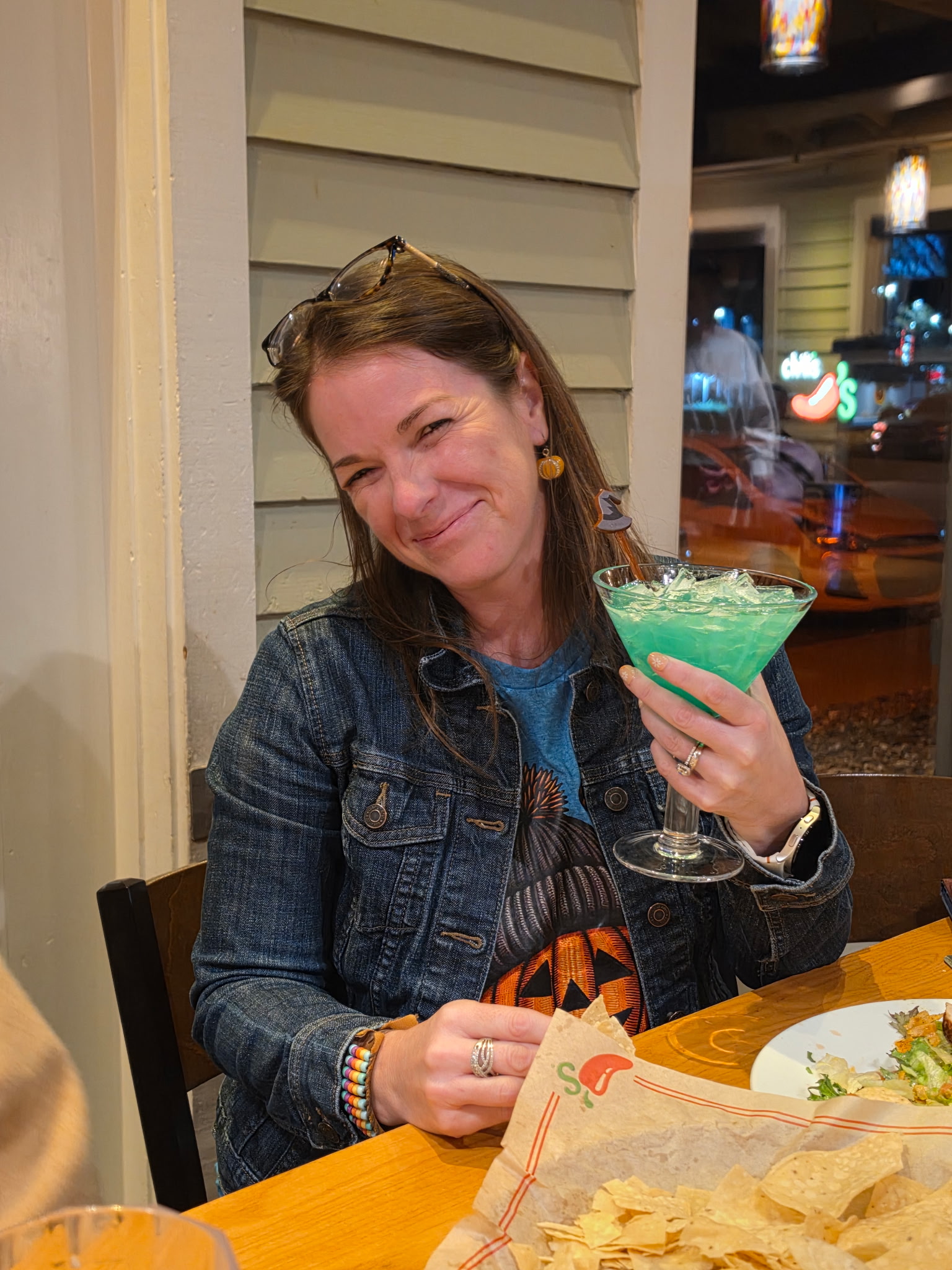 The author smiling at a restaurant dinner table and holding up a colorful margarita glass to celebrate.
